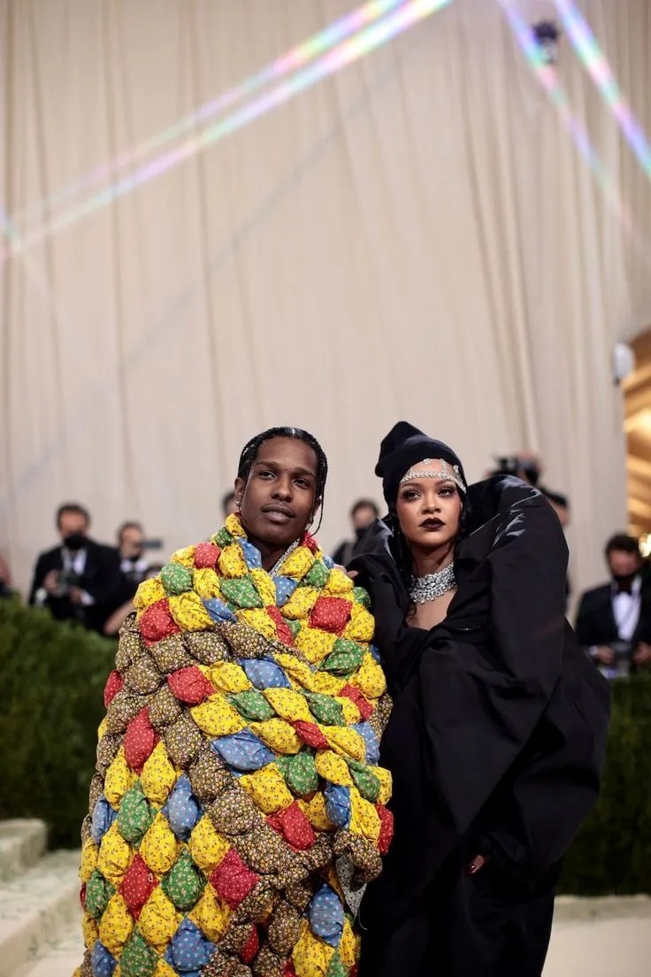 This may contain: two people standing next to each other in front of a white wall wearing colorful blankets